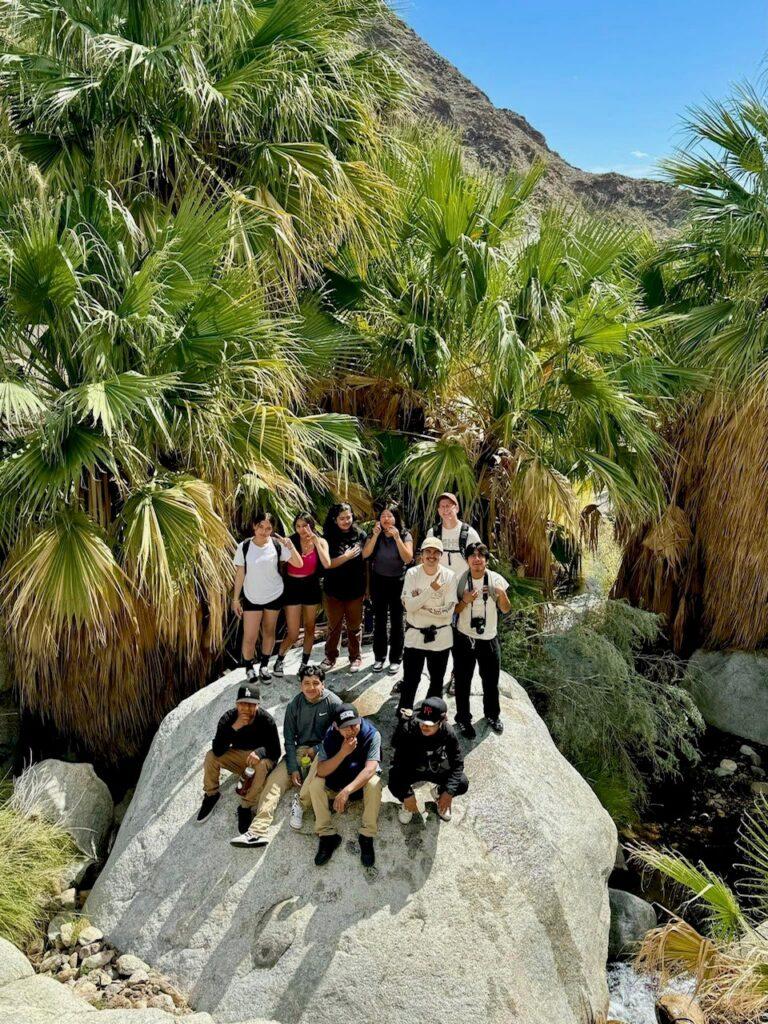Todd standing on large boulder in Palm Canyon next to palm trees with FamCamp participants.