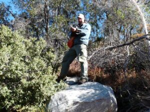 Scott standing on a large boulder near tress holding a kangaroo rat